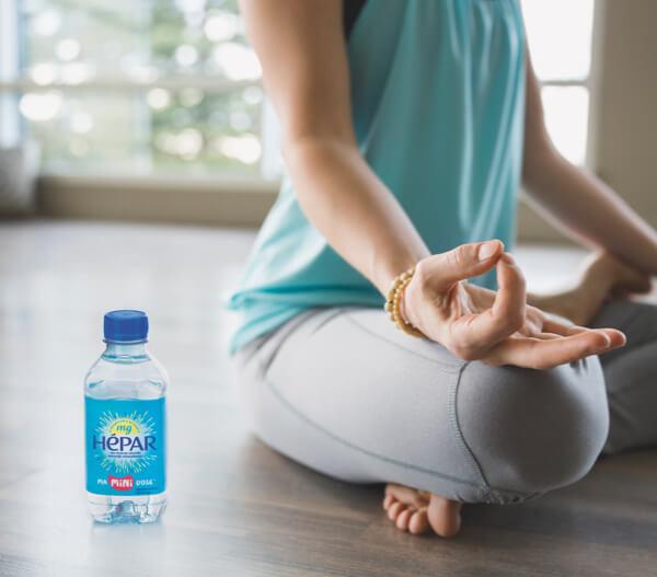 Unz petite bouteille d'eau Hépar et une femme faisant du yoga